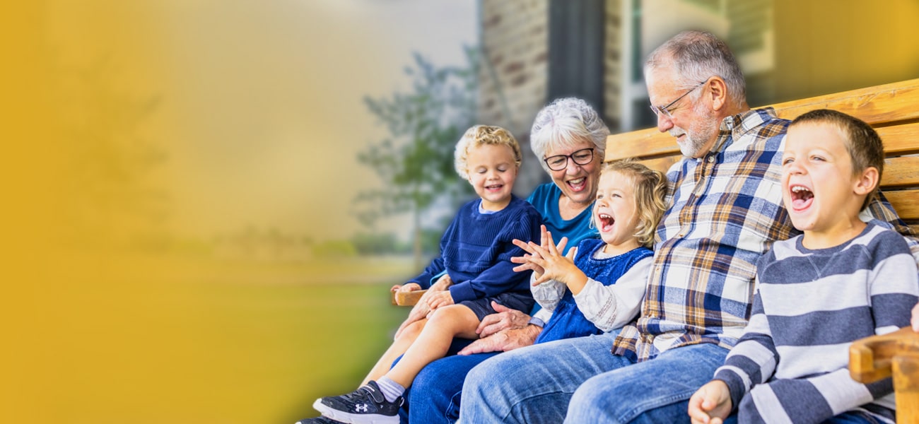 Smiling grandparents sitting on outdoor bench with their three grandchildren.