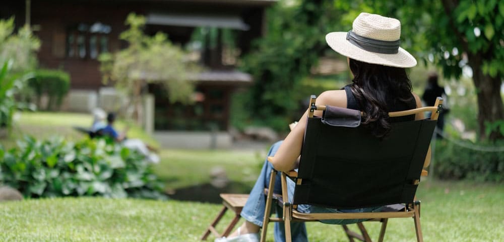 Female homeowner with hat sits out on lawn on a warm, sunny, summer day.