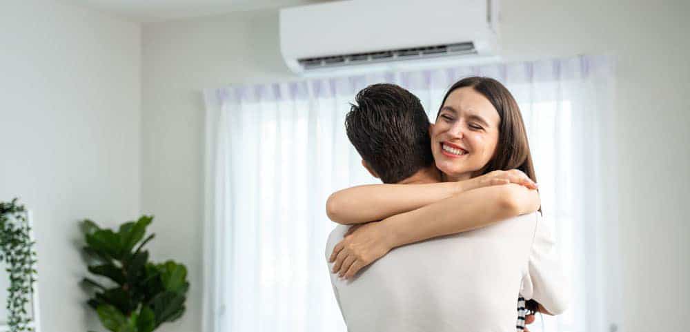 Male and female homeowner embracing with smiles in living room underneath their ductless system.
