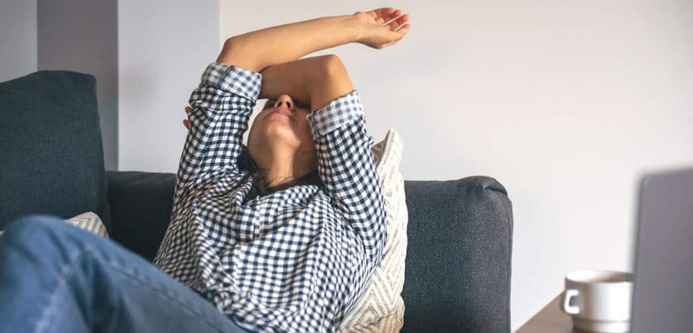 Frustrated female homeowner lays back on couch with arms thrown over her eyes.
